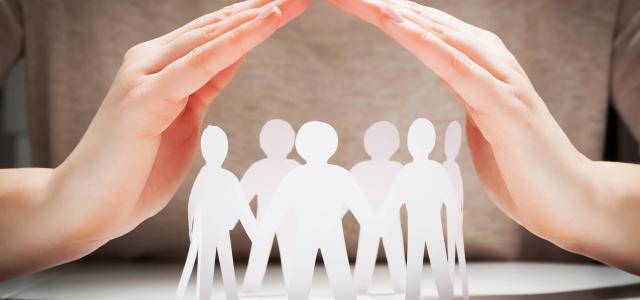 Paper people under hands in gesture of protection